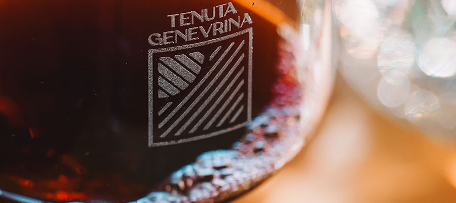 Dettaglio di un bicchiere marchiato Tenuta Genevrina pieno di vino rosso